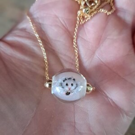 Custom white pet portrait necklace held in Claudia's hand